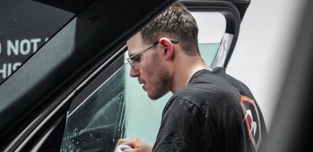 Technician squeegeeing window tint film onto a vehicle door window in an indoor install bay