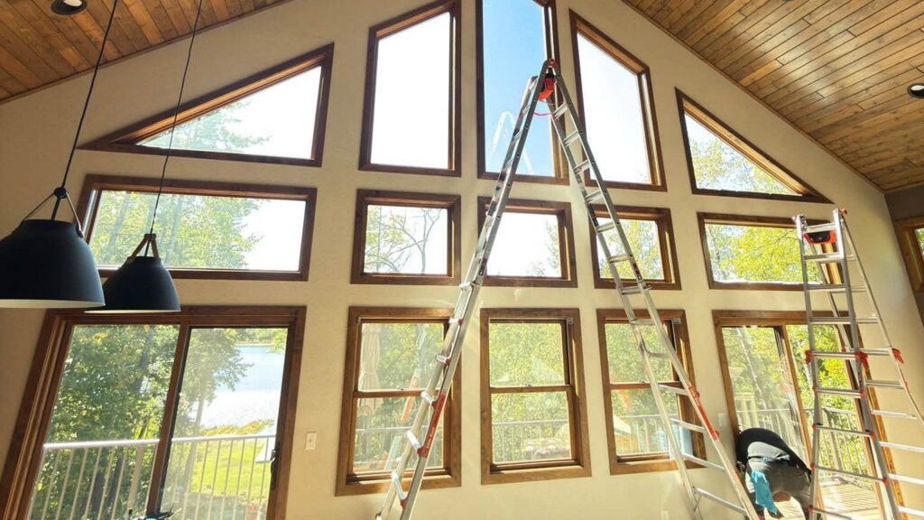 Sun Control installers applying window film to a two-story wall of windows in a Minnesota lake home