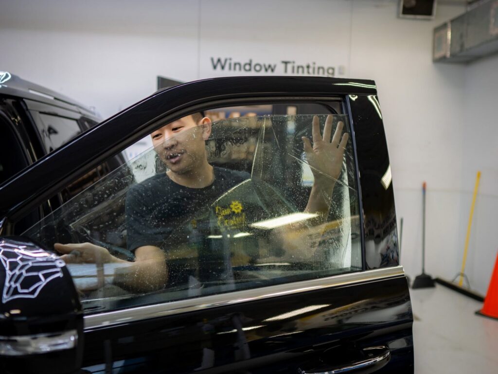 Sun Control technician applying window tint film to an SUV door window in an indoor install bay