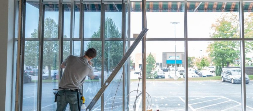 A technician applies window film inside a commercial space under construction, with one window section visibly darker from the tint. This image illustrates how visible light transmission (VLT) affects light levels and privacy based on film percentage.